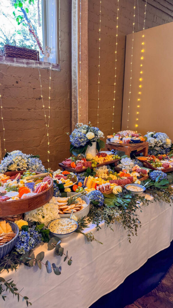 Oly Grazers charcuterie grazing table with cheeses, meats, fruit, crackers, and fresh flowers for a bridal celebration